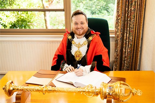 Mayor of Rushmoor 2025-26 Councillor Calum Stewart in his robes, sitting at his desk