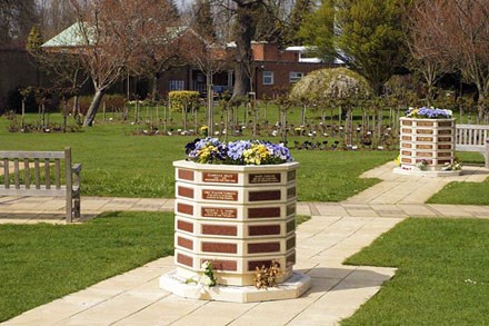 An octagonal memorial planter with flowers in the top, on a path in the crematorium grounds